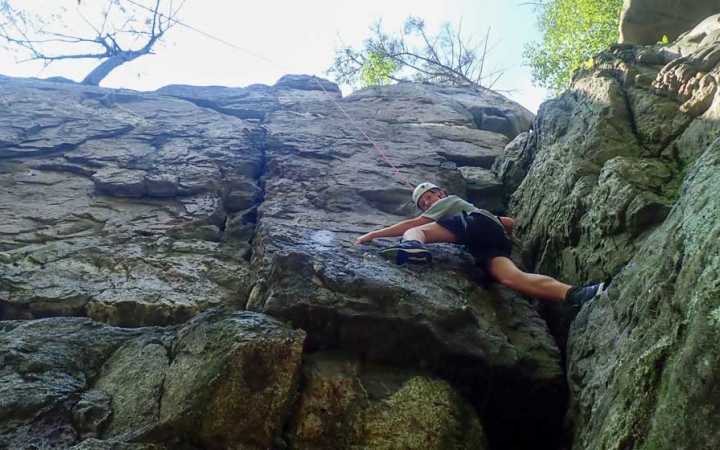 a teen scales a rock wall on a rock climbing trip with outward bound